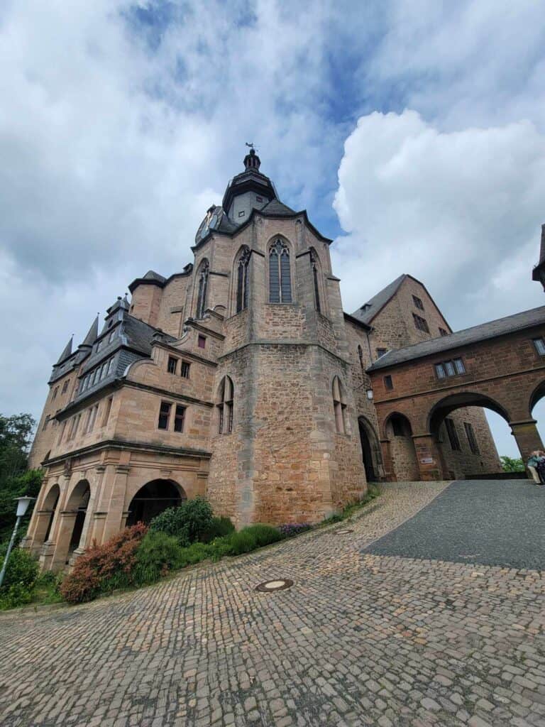 A large brownish sandstone castle with tall rounded windows and an arched passageway