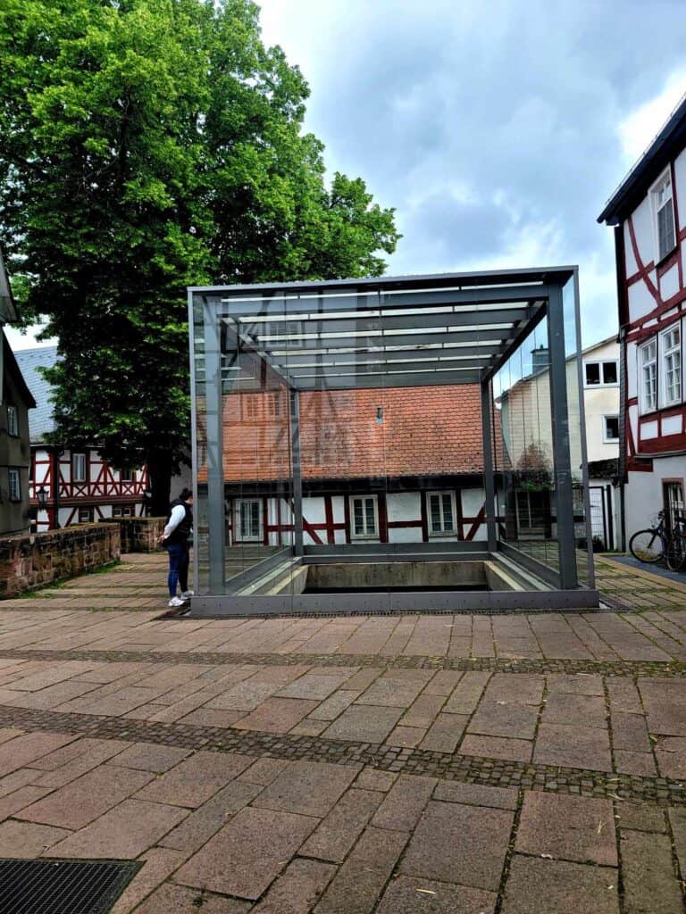 A large glass cube from the side. A hold in the plaza is visible underneath