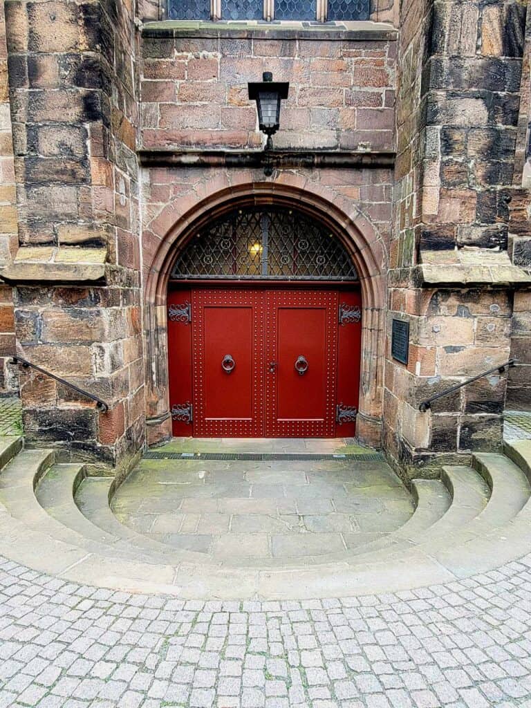 A large double red door with rounded transom window sits at the bottom of rounded stone steps