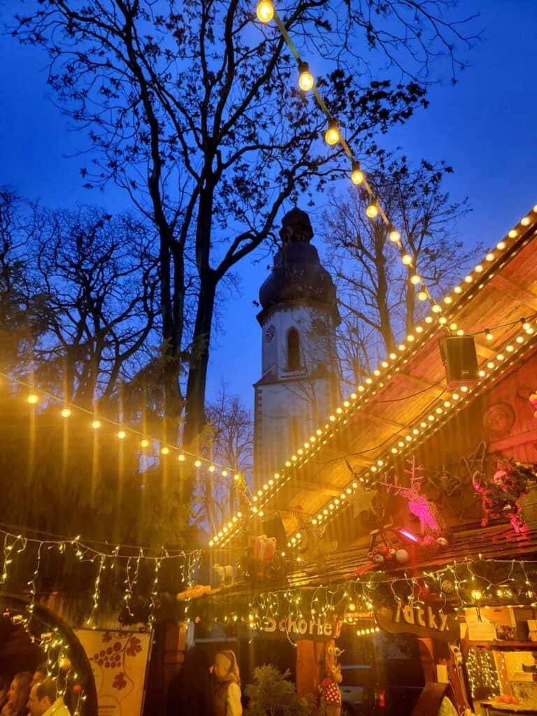 A market stall decorated in white lights with a church tower behind