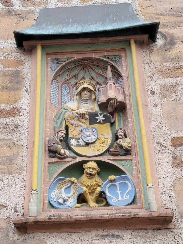 A carving of a woman holding a shield and a church above a lion-monkey holding two shields in blue