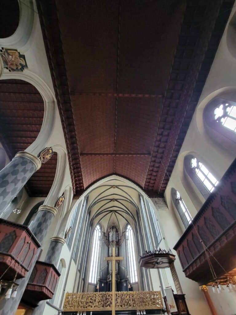 The wooden ceiling of a church with tall windows and columned arches on the side