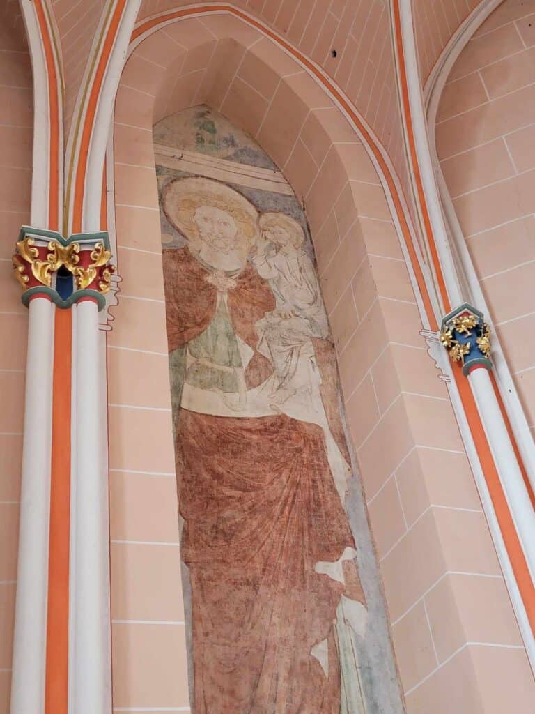 Pink stone blocks form a tall thin arch with a Medieval fresco of a religious figure with a halo holding a crown and the baby Jesus