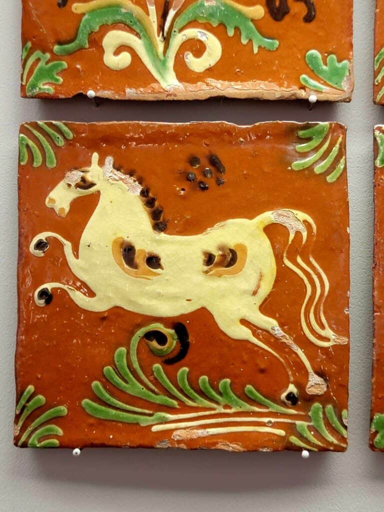 A bright orange tile with green embellishments and a white horse rearing in profile