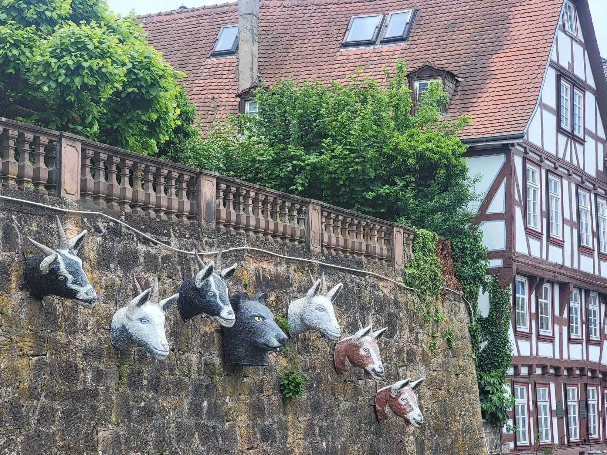 A stone wall with the sculptured heads of six goats and a wolf looking out