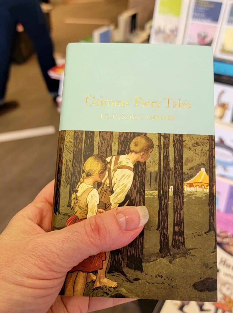 A woman's hand holding a small copy of Grimm's Fairytales