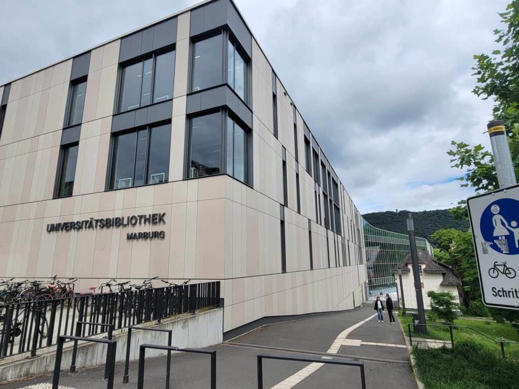 A modern white building with tall glass windows and Bibliothek Marburg on the side