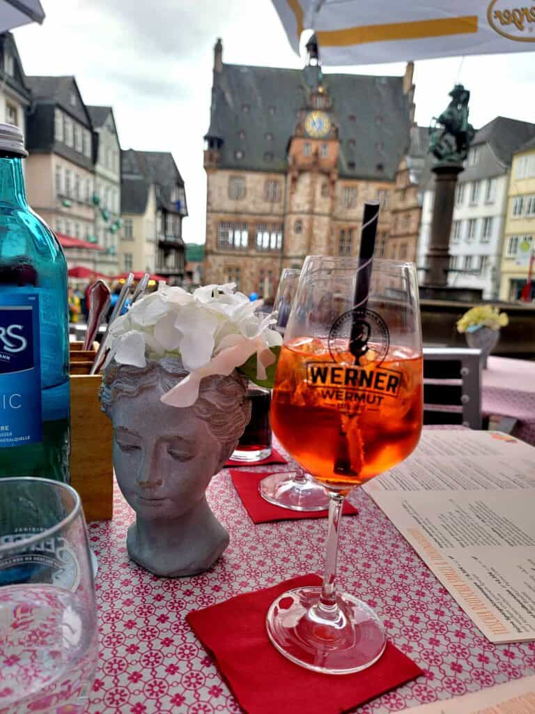 An Aperol spritz on a red napkin and a red tablecloth with the town hall in the background