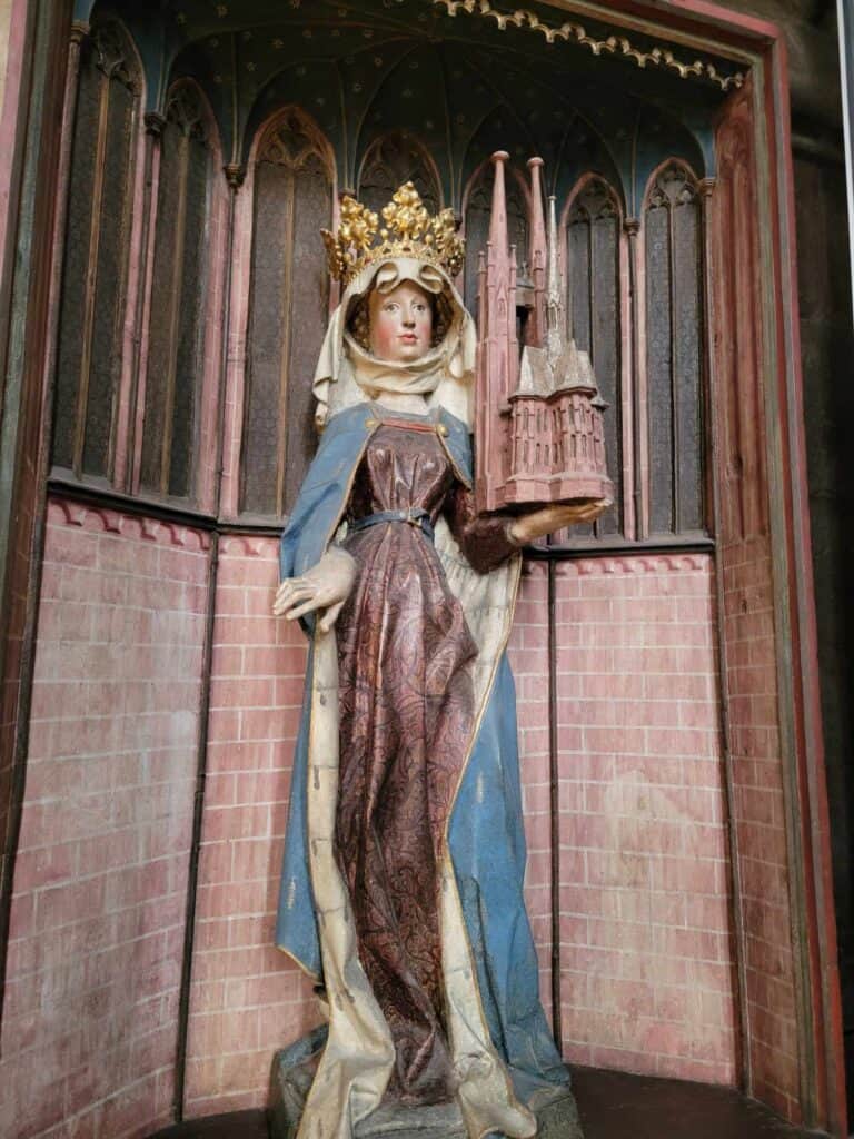 A woman in a crown and blue robe holds a model of the church