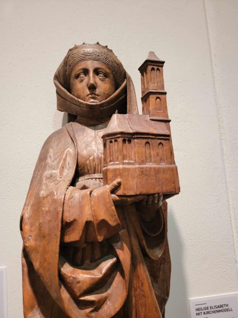 A Medieval wooden carving of a woman in a veiled headgear holding a church