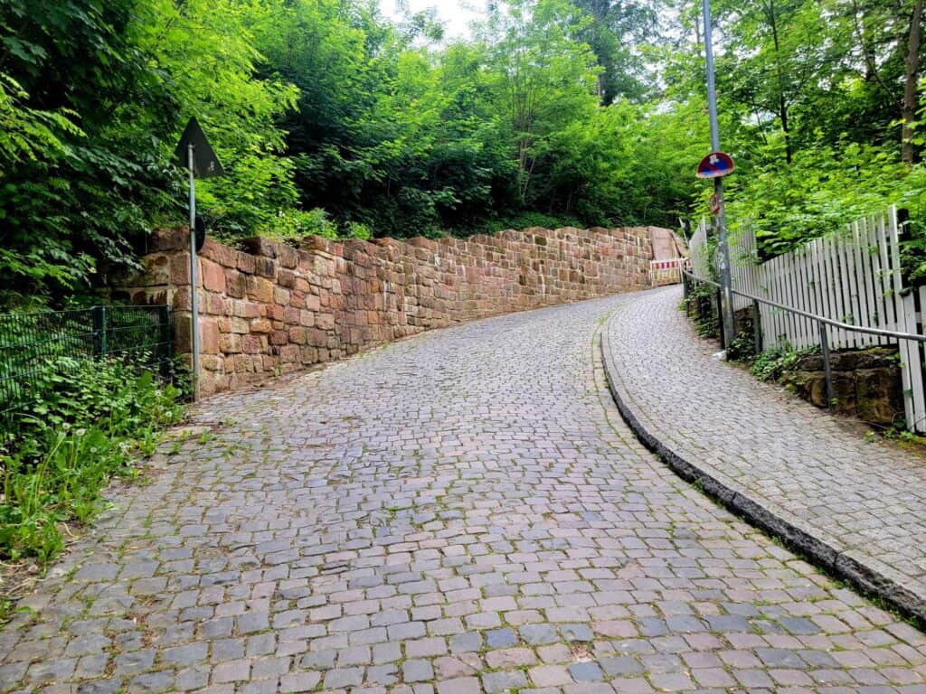 A fairly steep cobblestone road next to a stone wall bends out of sight