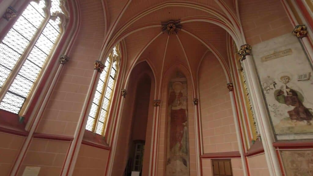 A pink room with tall leaded glass window and vaulted ceiling