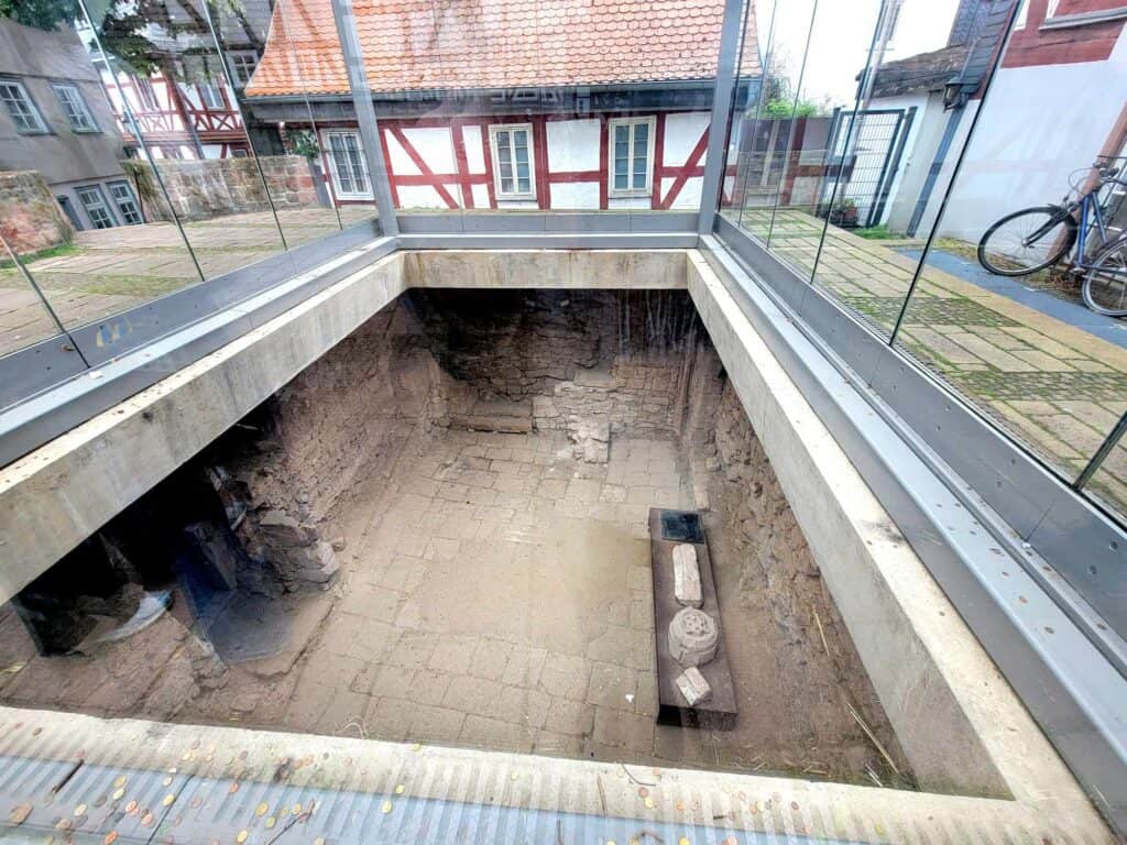 Looking into a square hole showing below street level - a floor and foundation walls and some pieces of stone decorative trim