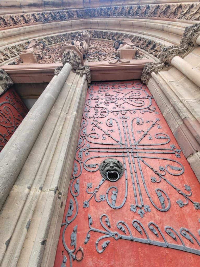 A tall red door with iron embellishment and a lion head door handle