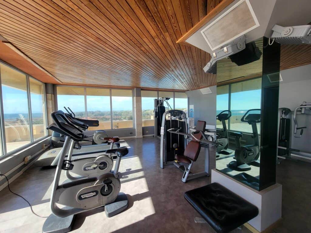 Gym equipment including exercise bikes in a room with lots of windows overlooking the ocean