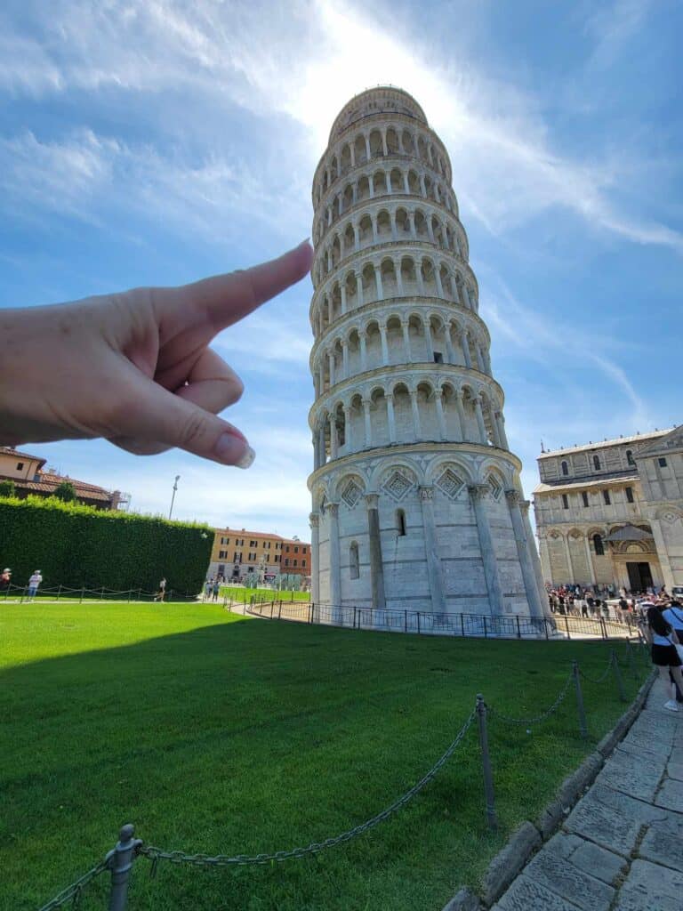 A hand with index finger outstretched appears to be holding up the Leaning Tower of Pisa