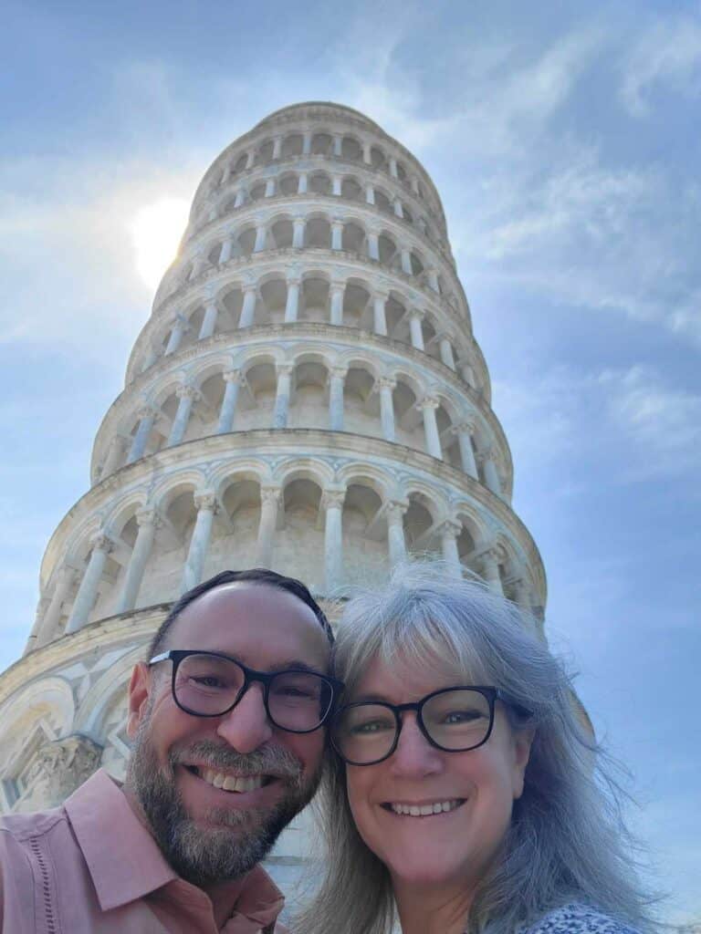 A smiling couple with the leaning Tower of Pisa immediately behind