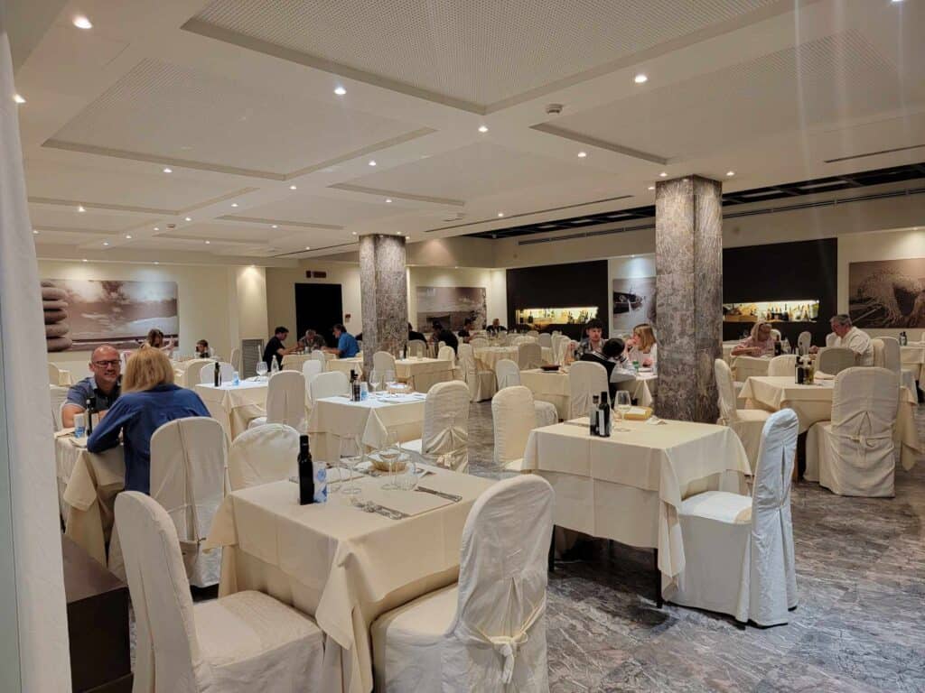 A hotel dining room with tables and chairs covered in cream-colored linens and set for dinner