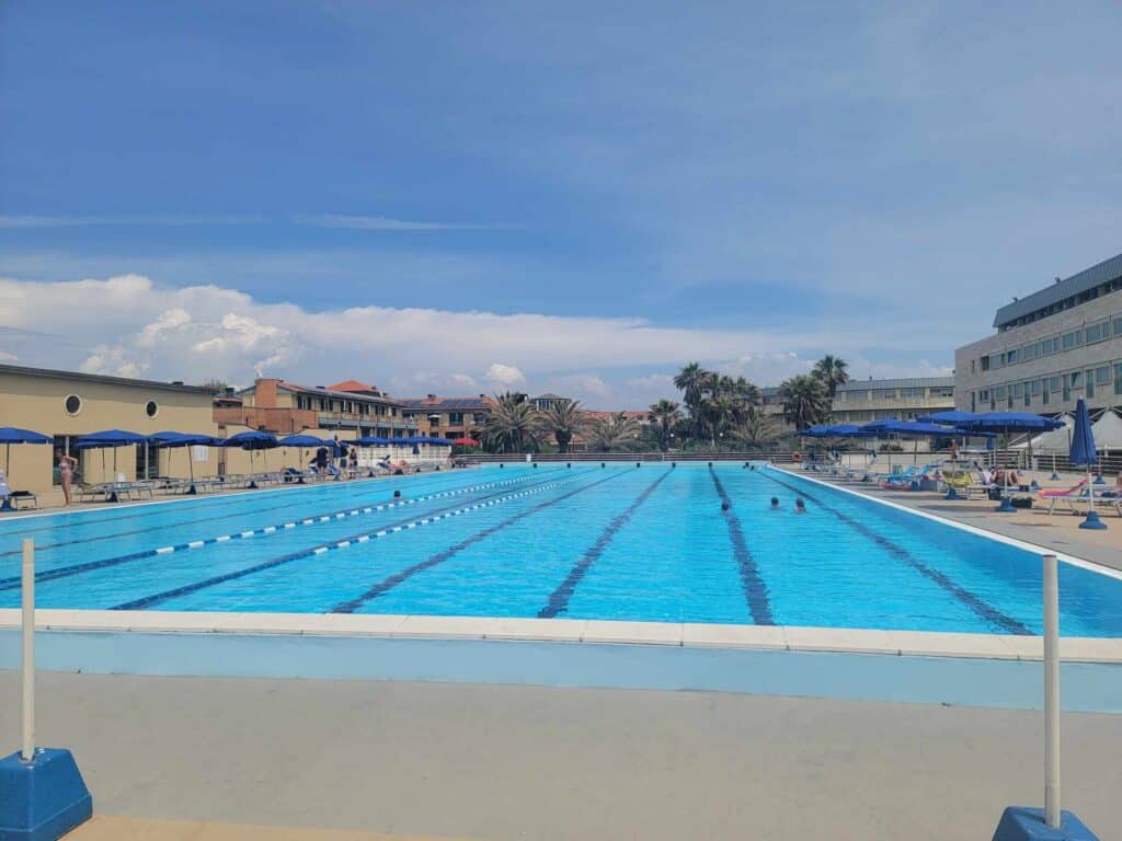 A large Olympic-sized swimming pool with a few people swimming