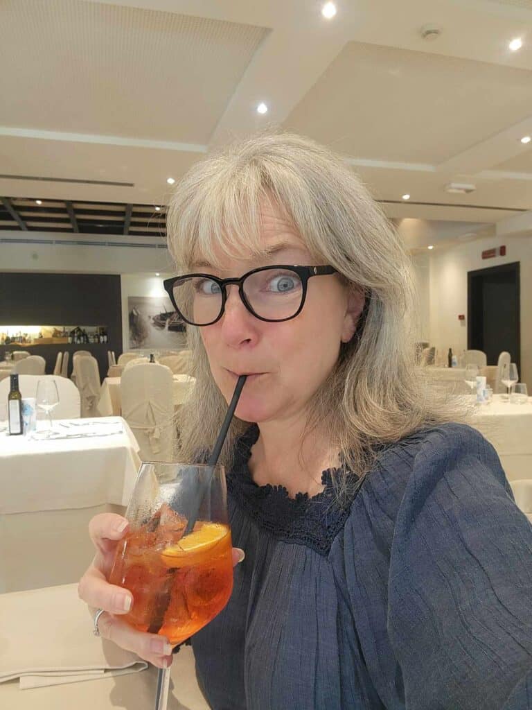 A woman sipping an Aperol spritz from a black paper straw