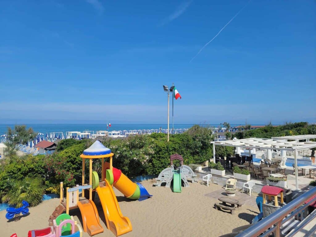 A kid's play area with slides, and sand, and chairs, and the ocean in the background