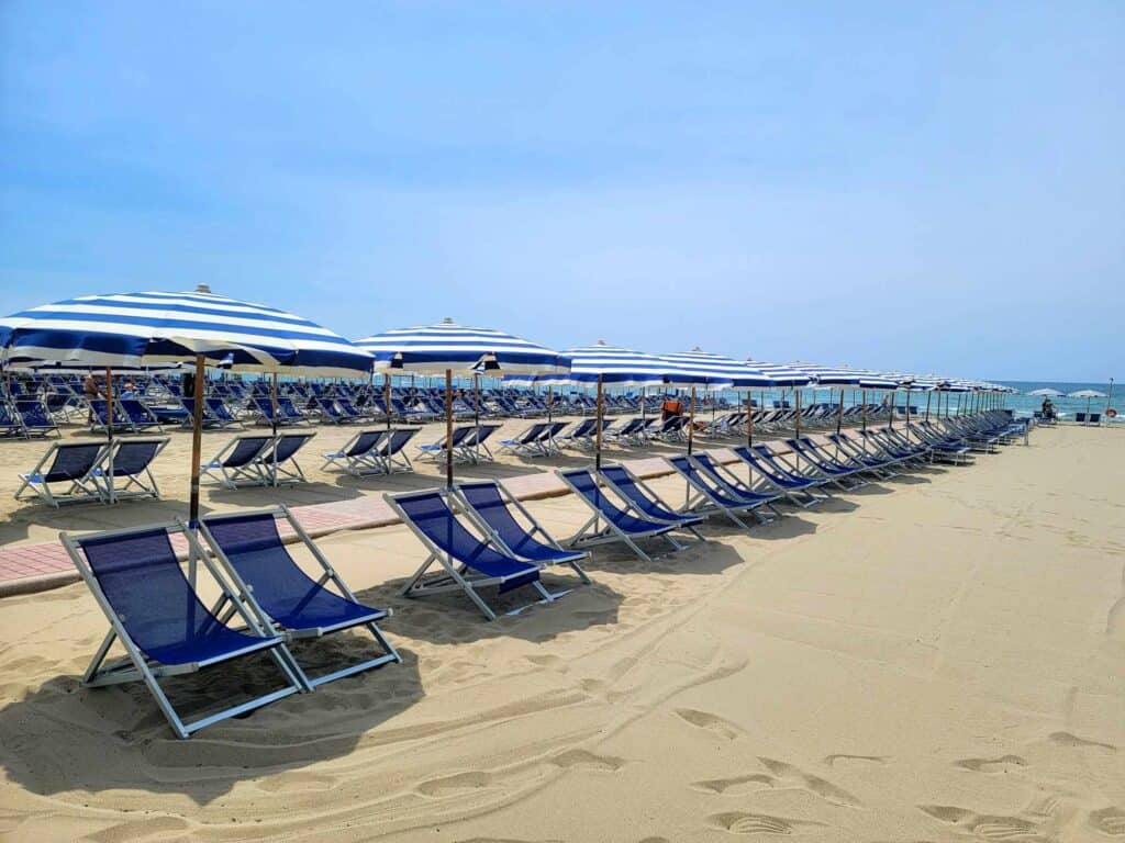 The blue lounge chairs and striped blue and white umbrellas all in a row on the sand belonging to the Grand Continental Hotel Tirrenia