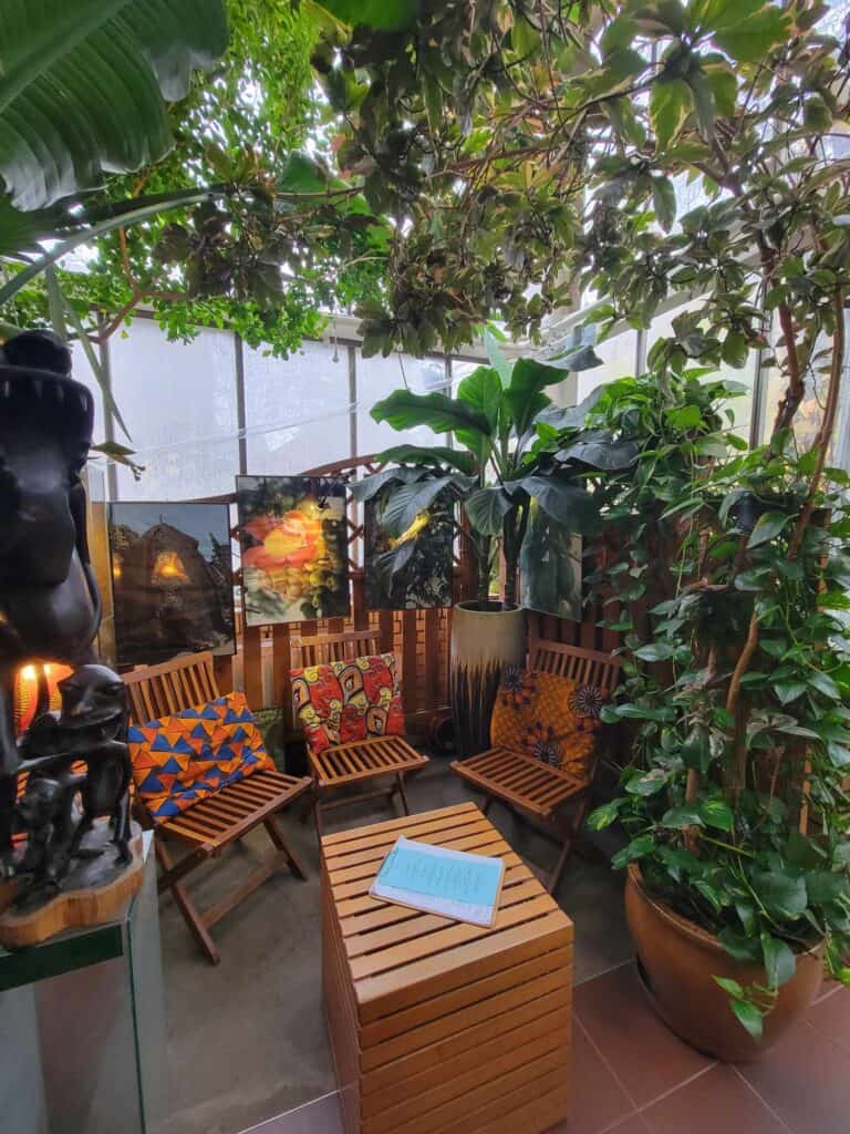 A room filled with jungle foliage, a wooden slatted table, and three wooden chairs