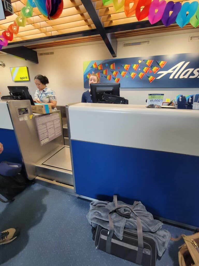 The Alaska Airlines counter at the airport with a dog carrier sitting on the floor