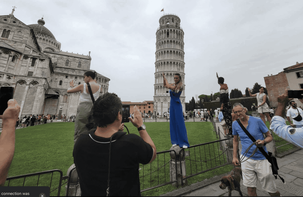 A man taking a picture of a woman standing on a railing posing for a picture in front of the tower