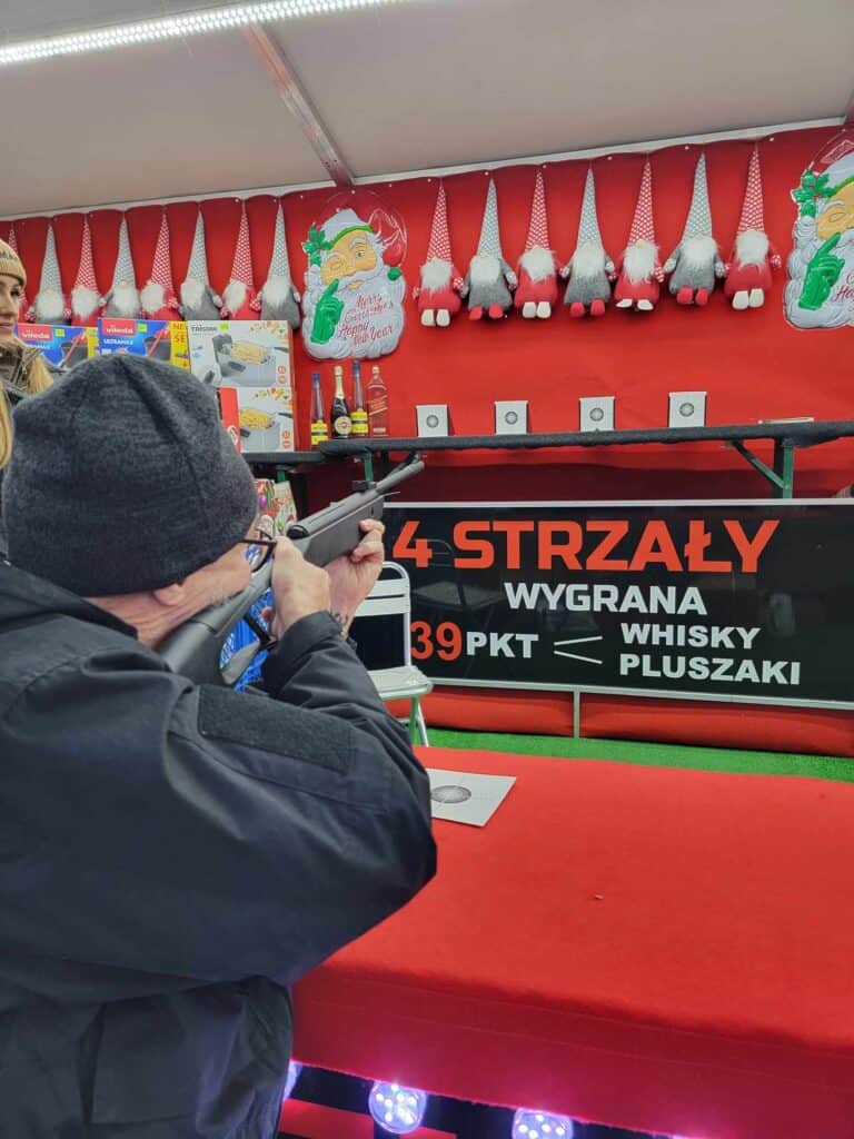 A man takes aim at a targe with a bb gun. A row of stuffed gnomes stretches out above a line of targets