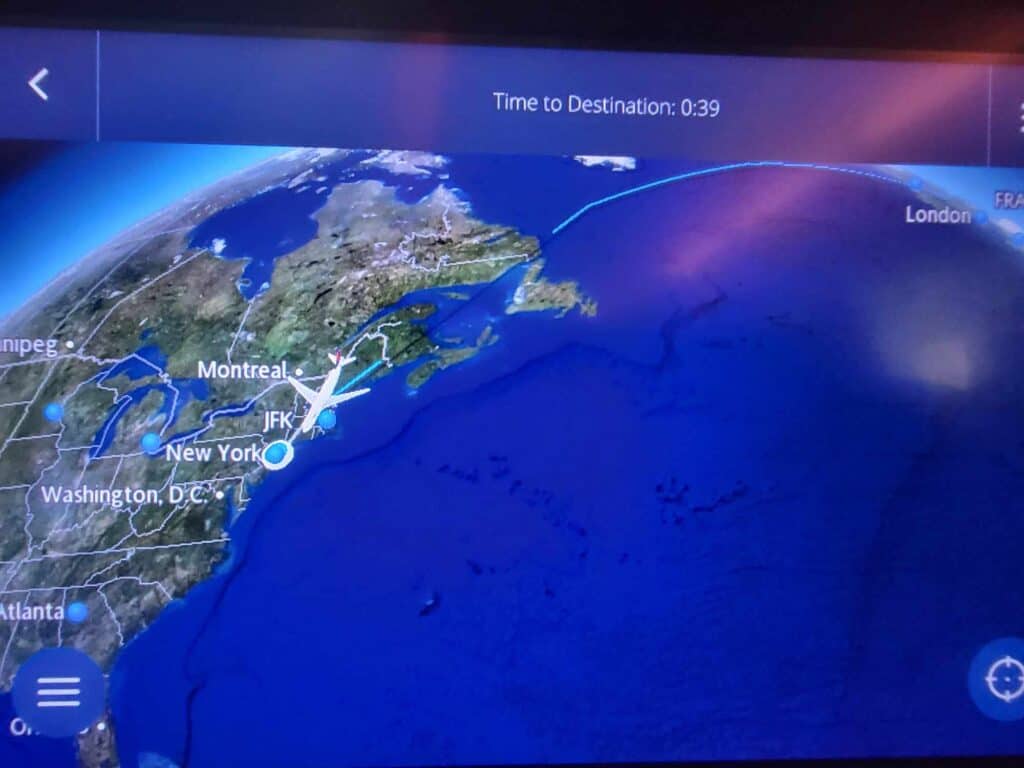 A flight screen on an airplane showing a plane on a map about to land at JFK airport in NYC