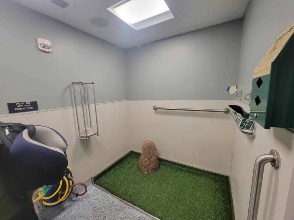 A dog relief area with a patch of astroturf, a fake boulder, a poop bag dispenser