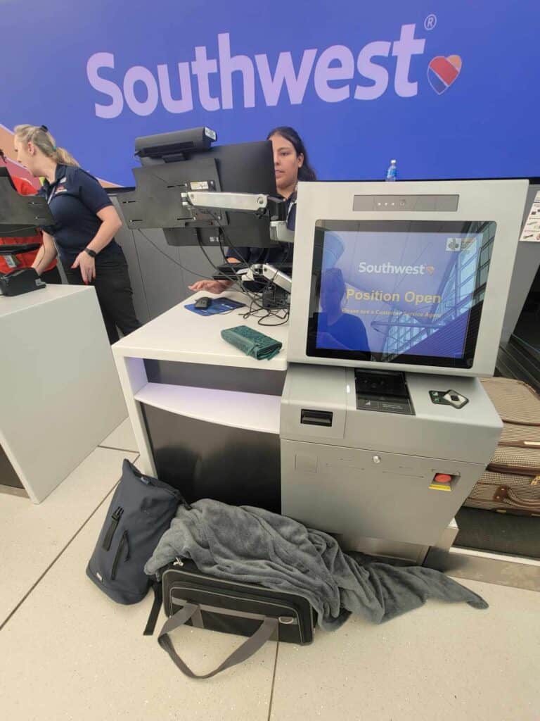 A dog carrier and backpack sit next to the check in kiosk for Southwest airlines while a gate agent looks at a computer screen