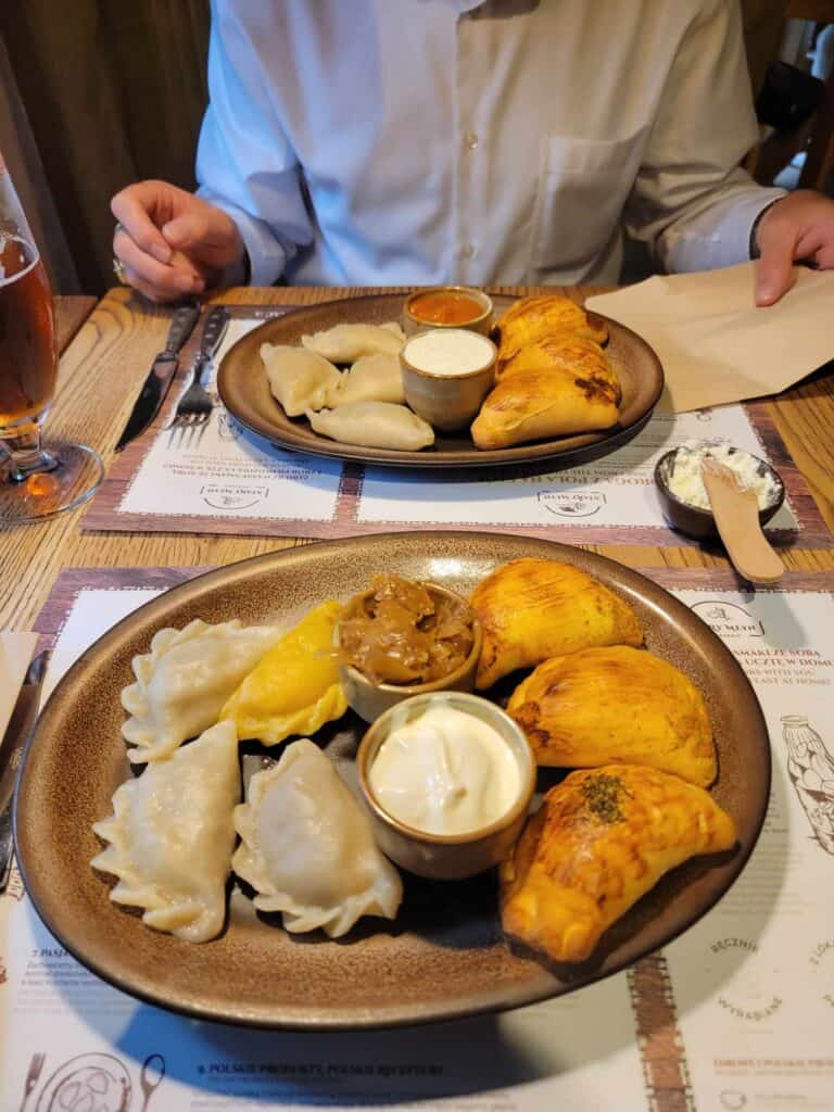 A plate of pierogies with cups containing onions and sour cream