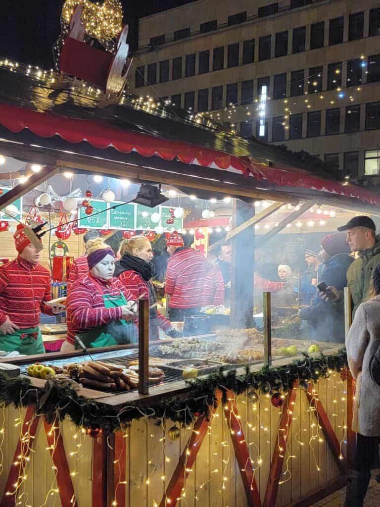 Four servers in red and white striped sweaters cooking and serving up sausages from a market stall