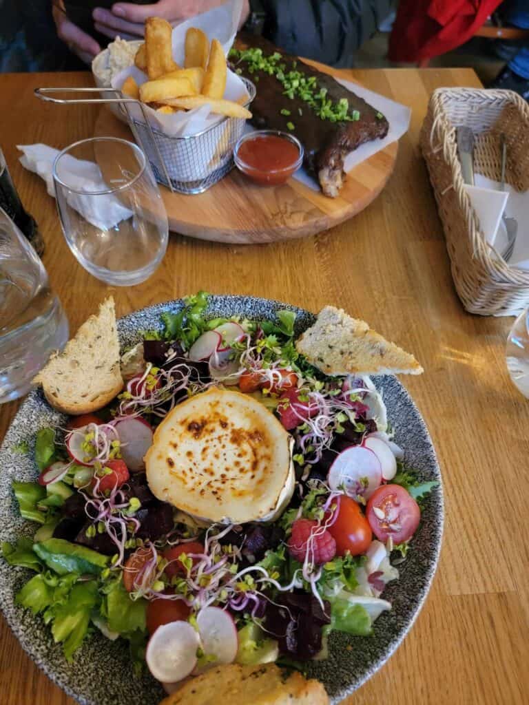 A colorful salad with a large goat cheese wheel in the center