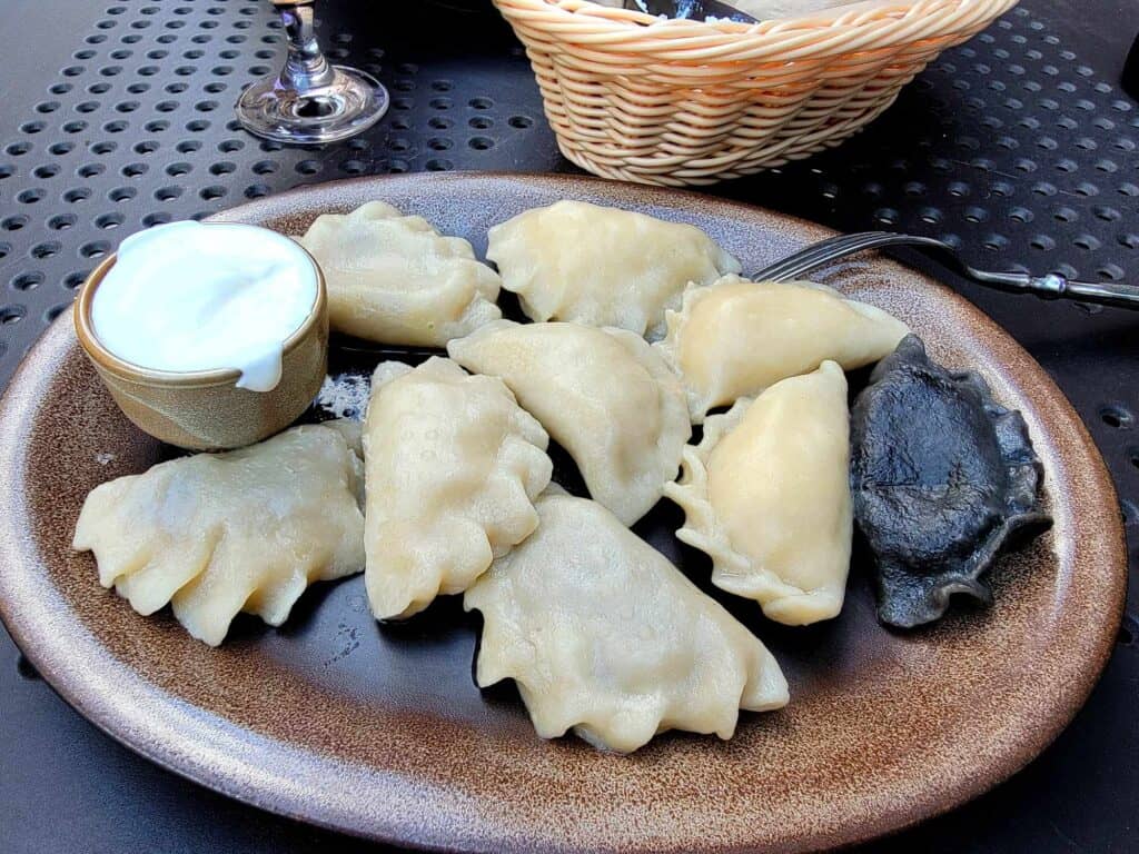 A plate of 9 pierogi Polish dumplings, one with black dough, and a cup of sour cream