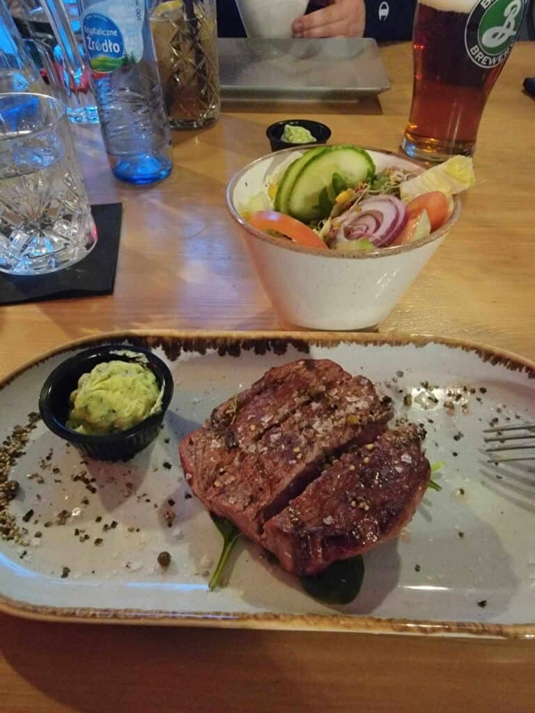 A steak on a plate with cracked pepper and a cup of butter