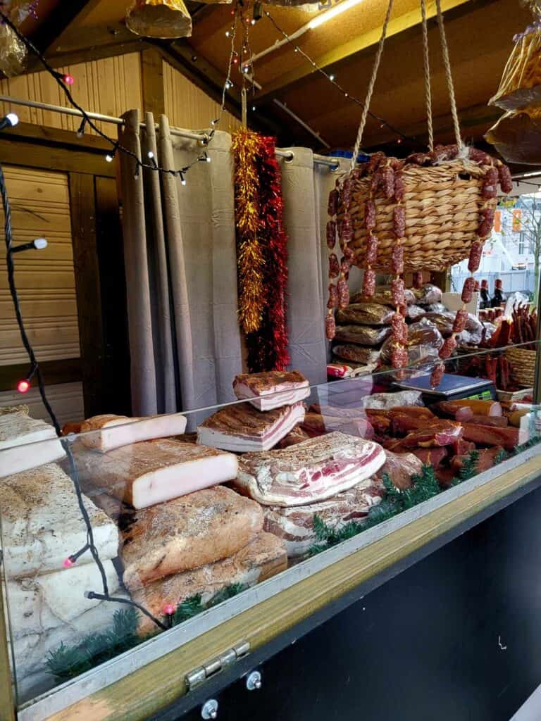 Rows of cured meats in a case, with some hanging behind in a basket