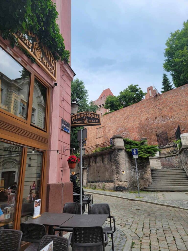 A red sandstone building with a black table and chairs outside on the cobblestones