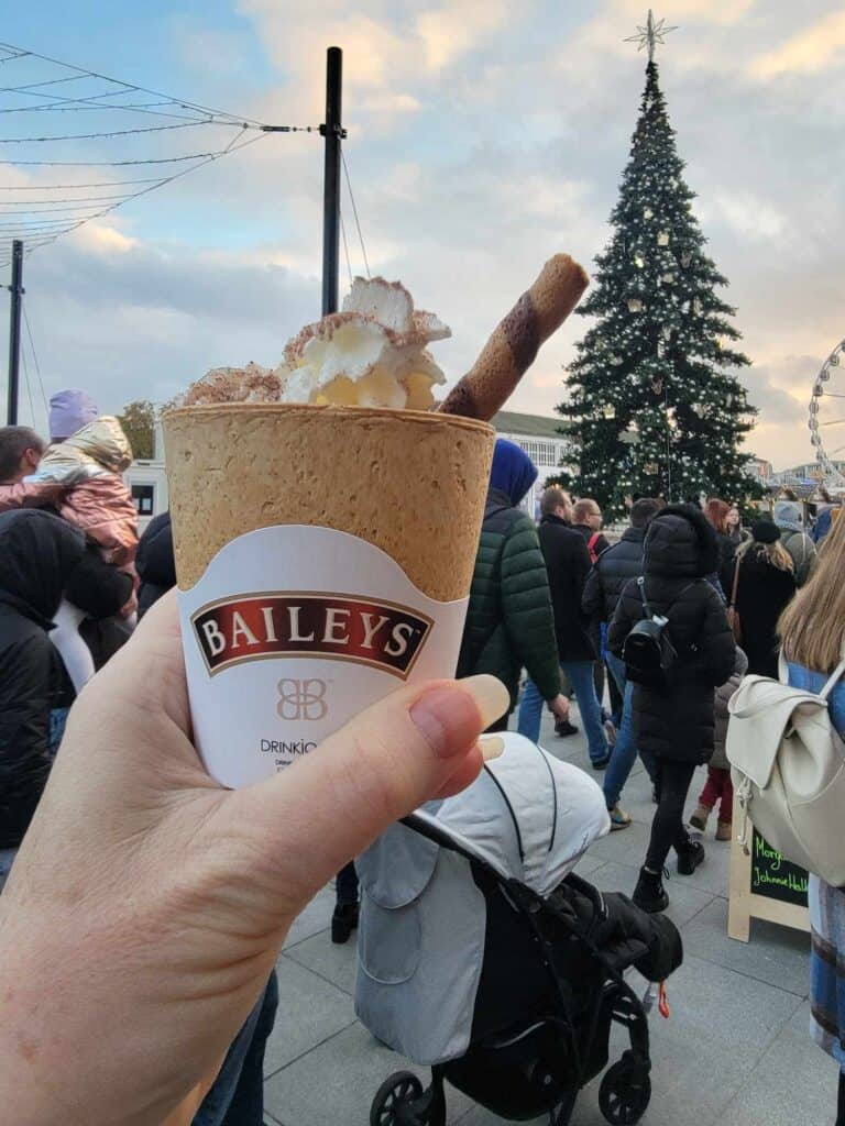 A woman's hand holeing up a cup of warm Bailey's with whipped cream and a thin tubular cookie