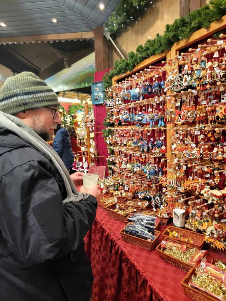 A man in a knit hat and scarf looks at a wall of wooden Christmas ornaments