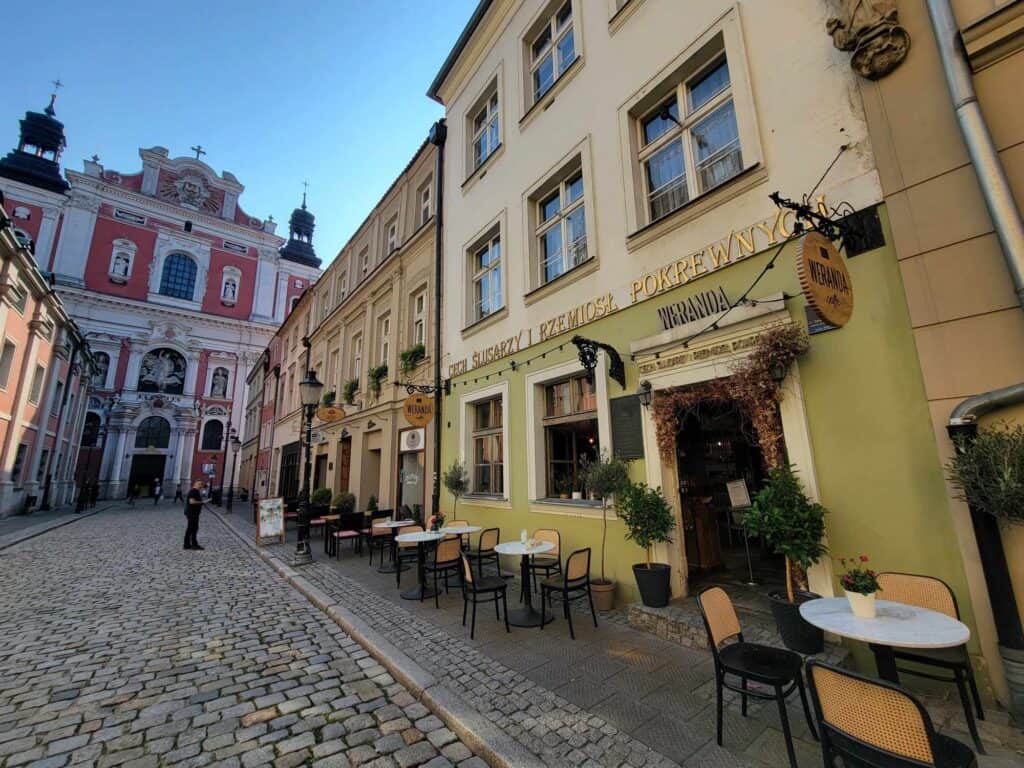 An elaborate baroque church in dark pink and white, a cobblestone street with a cozy cafe