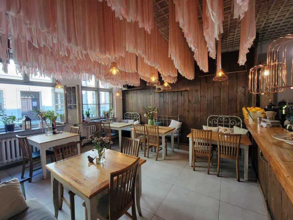 Cafe tables with wooden chairs, vases of flowers, white wrought iron details and thousands of strips of pink fabric hanging from the ceiling