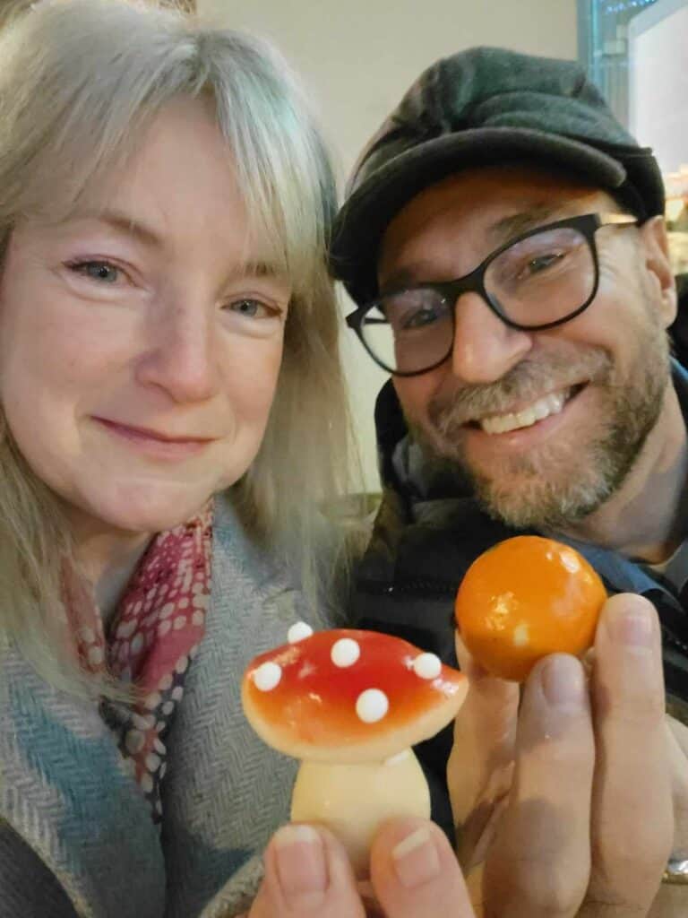 A couple with marzipan, smiling. she has a toadstool, he has an orange