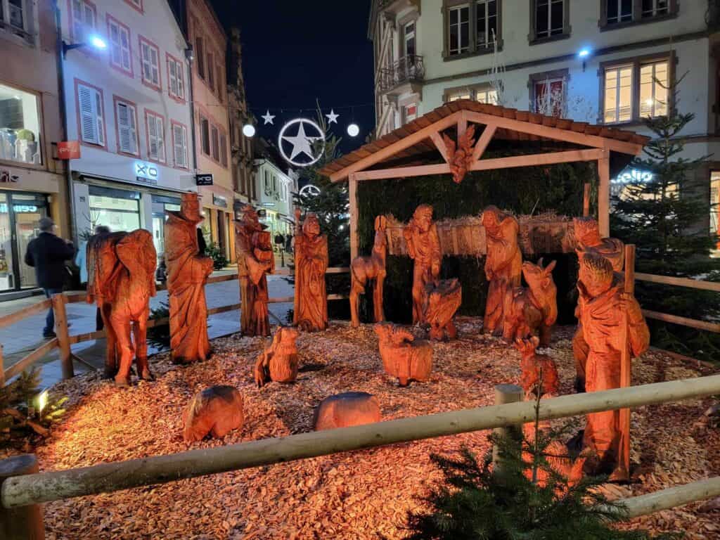 A life-sized carved wooden nativity scene next to a street decorated with stars