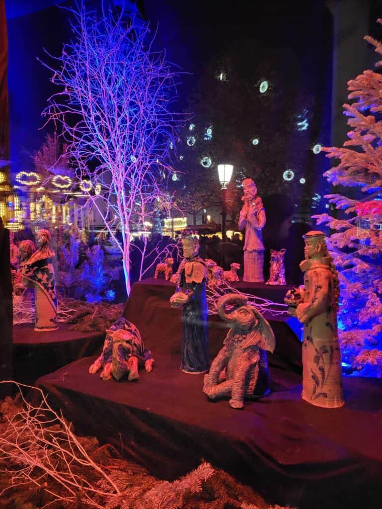 A large nativity scene illuminated in blue and red flanked by snow covered trees