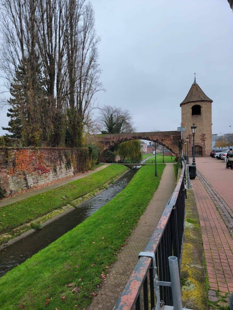 A small cement canal with a stone bridge over it connected to a tower with a pointed top on one side