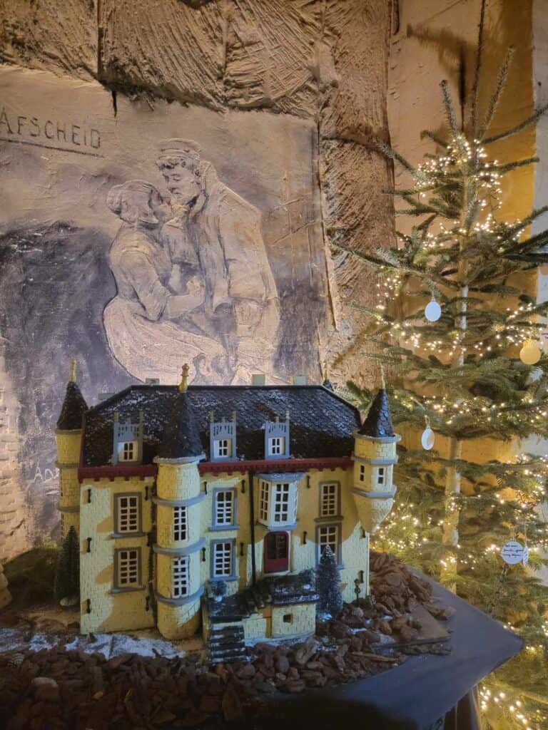 A model of a castle next to a Christmas tree with white lights in a limestone cave