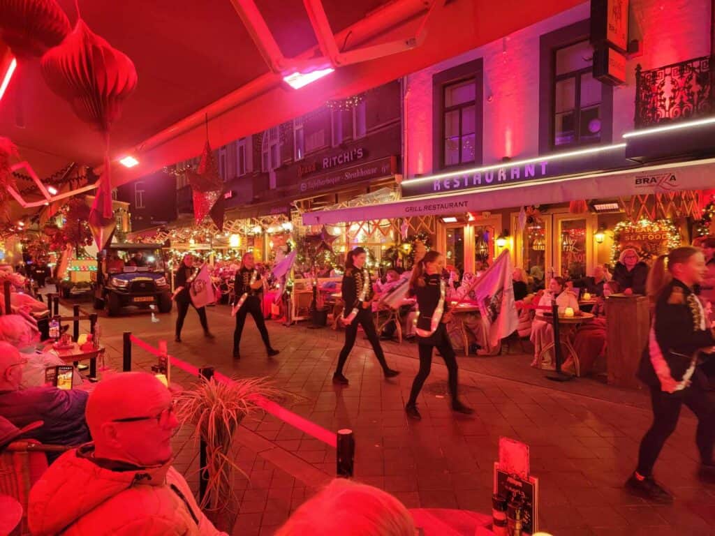 A row of kids in black unitards and gold sashes marching down a street bathed in red light